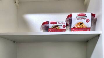 Un estante de cocina con una caja de Rubbermaid Take Alongs, un recipiente blanco y tazones apilados.