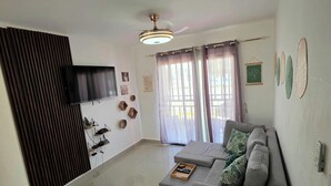 A living room with a grey sofa, a flat-screen TV mounted on the wall, and a ceiling fan. - New! LaRomanaDR SecludedJourney (La Romana)