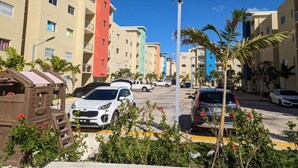 A multi-story residential building with balconies, parked cars, and palm trees. - New! LaRomanaDR SecludedJourney (La Romana)