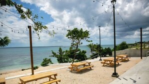 A beachside area with wooden picnic tables and benches, a clear view of the ocean, and string lights overhead. - New! LaRomanaDR SecludedJourney (La Romana)