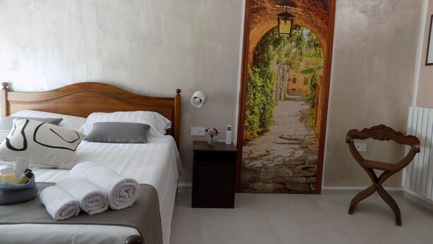 Une chambre à coucher avec un lit en bois, du linge de lit blanc, une table de chevet ornée d’un vase et un tableau représentant un sentier de pierres.