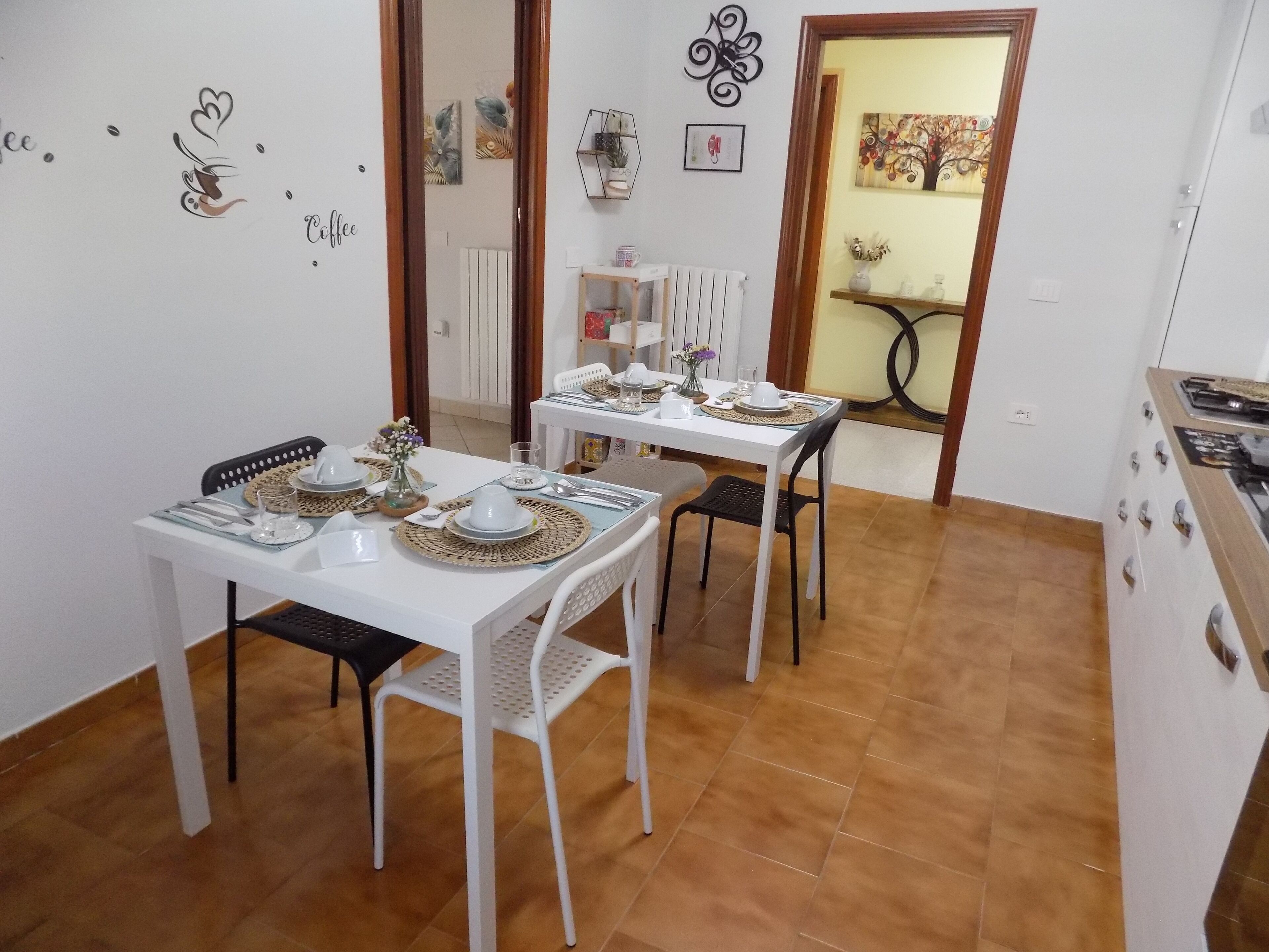 Un comedor con dos mesas blancas dispuestas para cuatro comensales, cada una con cubiertos y adornos.