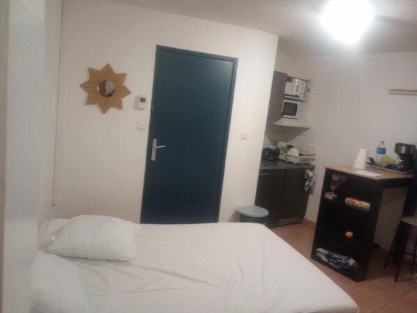 A small, simple room with a bed, a desk, and a kitchenette. - The Popes' Refuge (Avignon)