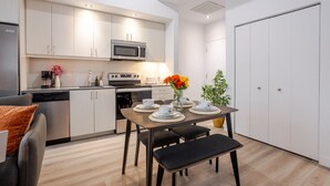 A modern kitchen with white cabinets, a microwave, stove, and a dining area with a table and chairs. - Elegant 1BR Retreat | Chic Stay in Old Port (Montreal)