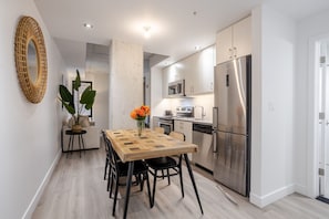 A modern kitchen with a dining area, featuring a wooden table, black chairs, a refrigerator, and a microwave.