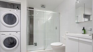 A modern bathroom with a glass shower enclosure, a toilet, and stacked washing machines.