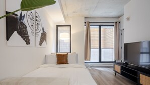 A modern hotel room with a large bed, a TV, and a window with curtains.