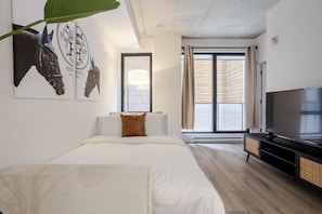 A modern hotel room with a large bed, a TV, and a window with curtains.