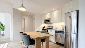 Een moderne keuken met een houten eettafel, stoelen, roestvrijstalen apparatuur en een hanglamp.