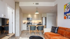 Een ruimtelijk ingerichte leefruimte met kitchenette, eethoek, bank en televisie.