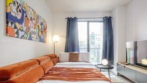 Een moderne hotelkamer met een groot bed, een bank, een televisie en uitzicht over de stad.