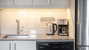 Een moderne keuken met roestvrijstalen apparatuur, waaronder een koffiezetapparaat, waterkoker en vaatwasser.