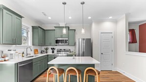 Une cuisine moderne avec des meubles de couleur verte, des appareils en acier inoxydable et un îlot central doté de tabourets de bar.