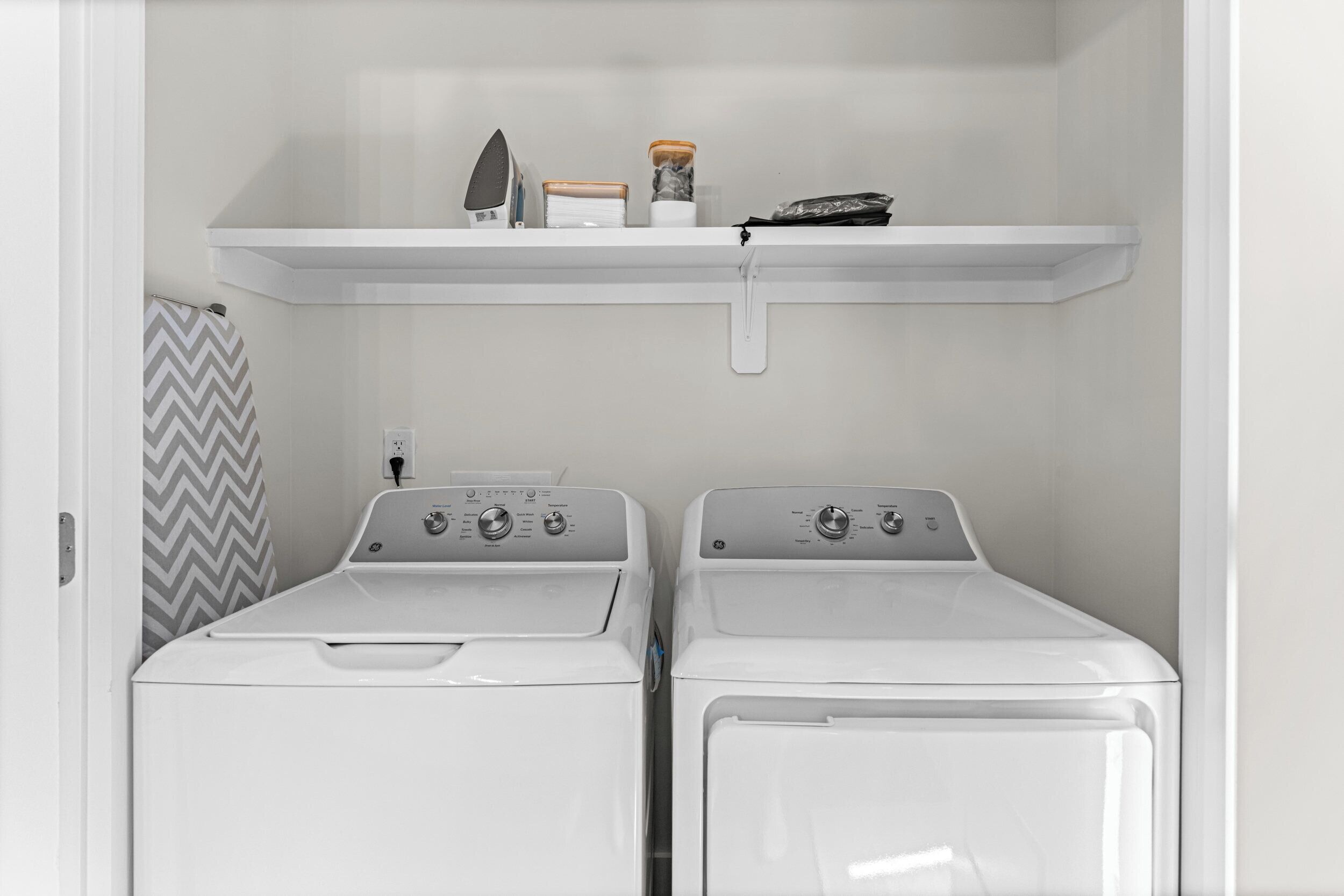 A laundry room with two front-loading washing machines and a shelf above containing a few items.