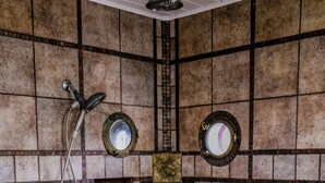 Ein gefliestes Duschbad mit Haltegriff, Duschkopf und kleinem Fenster.