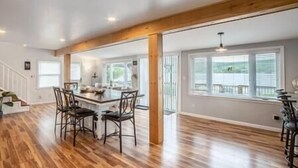 A spacious room with hardwood flooring, a central island with chairs, and large windows providing natural light. - Lake Front Reverie- Waneta Lake, NY (Dundee)