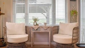 A room with two wicker chairs, a small table with a plant, and a window with blinds. - Lake Front Reverie- Waneta Lake, NY (Dundee)