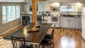 A modern kitchen with white cabinets, a large island, and a dining area with chairs. - Lake Front Reverie- Waneta Lake, NY (Dundee)