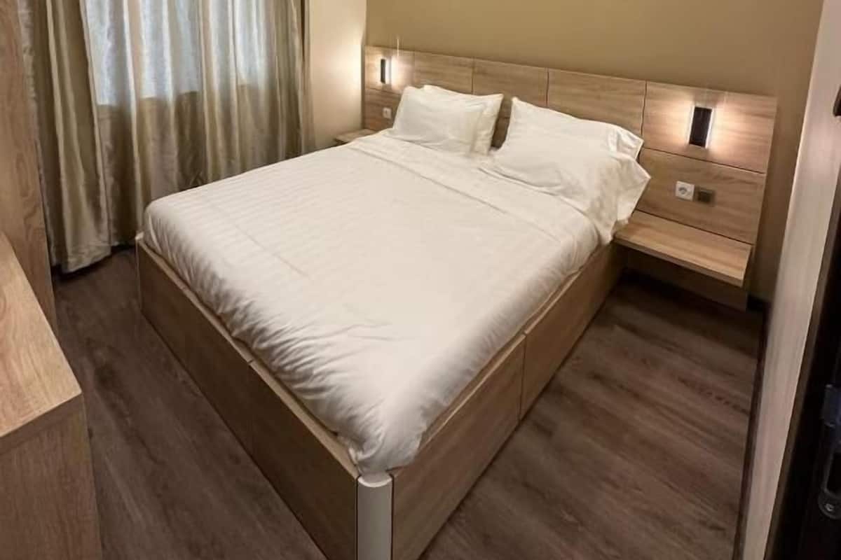 Ein modernes Schlafzimmer mit einem großen Bett, einem Holzkopfstück, Nachttischen und einem Vorhang am Fenster.