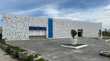 A modern building with a perforated facade, a blue vertical stripe, and a small landscaped area with a tree and plants.