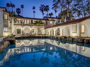 A pool with clear water reflecting the architecture, surrounded by a building with arched windows and balconies.