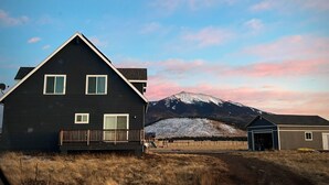 Una casa de dos pisos con fachada oscura, un deck de madera y una montaña al fondo.