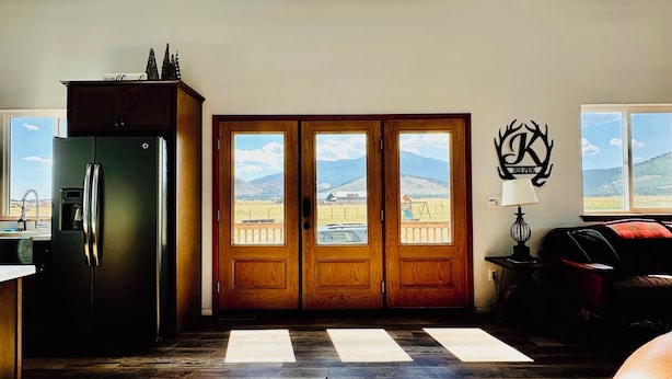 Amplia sala de estar con techo alto, ventanas grandes, una cocina con refrigerador y vista al exterior.