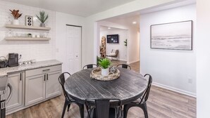 Una cocina moderna con armarios blancos, encimera de granito y un comedor con mesa y sillas de madera.