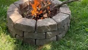 Un patio trasero con un hogar de piedra, dos sillas Adirondack azules y una terraza de madera.
