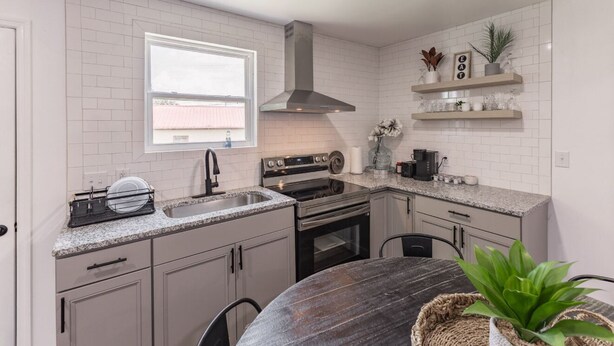 Una cocina moderna con azulejos blancos tipo metro, una campana extractora de acero inoxidable, un horno empotrado y un ventanal que proporciona luz natural.