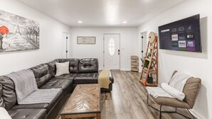 Una sala moderna con un sofá seccional de cuero, una mesa de centro de madera y un televisor que muestra servicios de streaming.