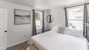 Un dormitorio con cama, un cuadro, una ventana con cortinas y un espejo.