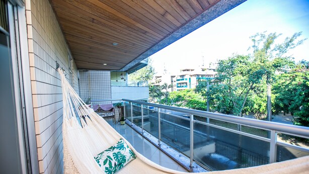 A balcony with a hammock, a railing, and a view of buildings and trees.