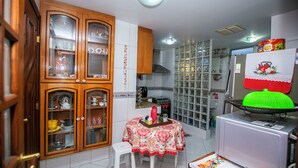 A compact kitchen with wooden cabinets, a dining table with a floral tablecloth, and a refrigerator with a green basket on top.