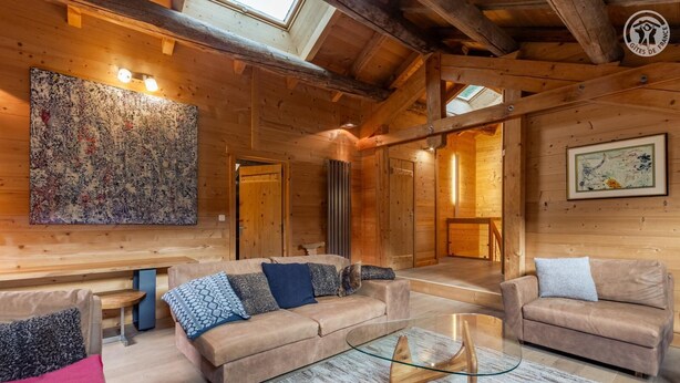 A cozy log cabin interior with a sofa set, a glass coffee table, and a large abstract painting on the wall.
