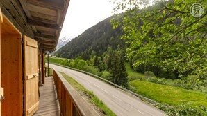 A wooden building with a balcony overlooking a road and forested hills.