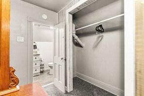 Een gang met een deur naar een badkamer, een kapstok en een klein wastafelgedeelte.