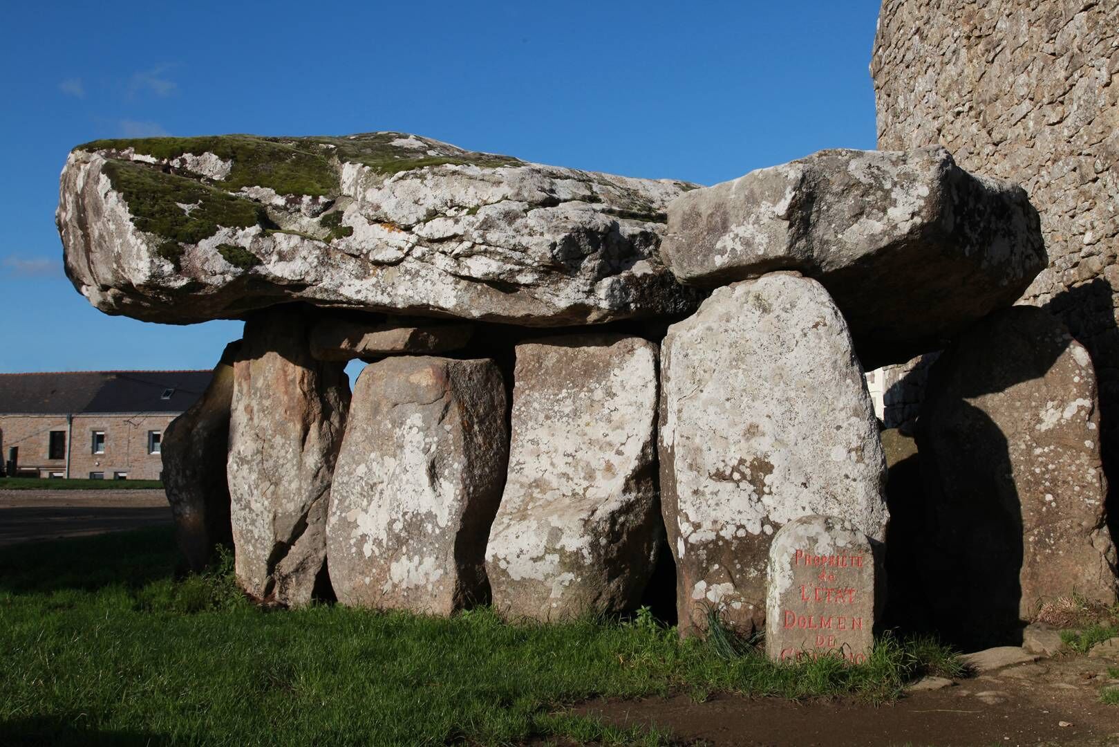 En stor stengrund struktur med inskriptioner, muligvis et historisk monument, beliggende udendørs med en bygning i baggrunden.