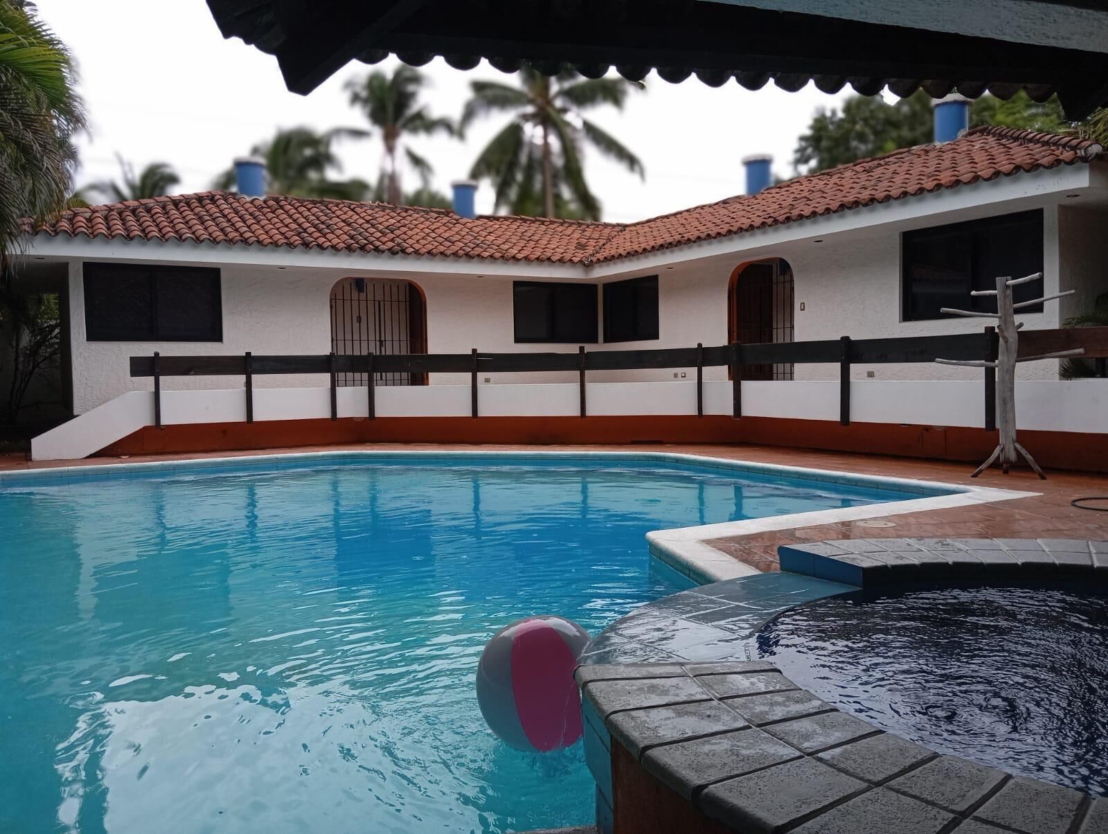 A swimming pool with a tiled deck, a hot tub, and a building with a tiled roof and arched windows.