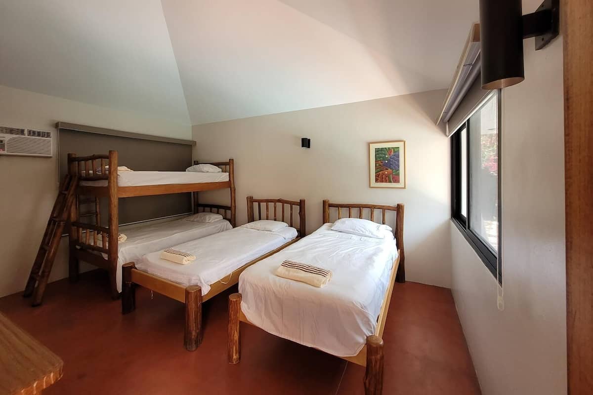 Ein Schlafsaalzimmer mit Etagenbetten, einem Holztisch, einem Fenster mit Blick und einer wandmontierten Klimaanlage.