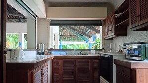 Une cuisine compacte avec des meubles en bois, un four à micro-ondes encastré et une fenêtre donnant sur un jardin tropical.