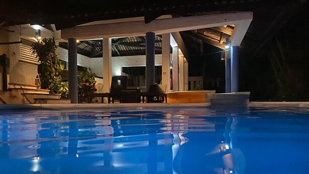 Une piscine dotée d’un espace de repos couvert et d’un bâtiment en arrière-plan.