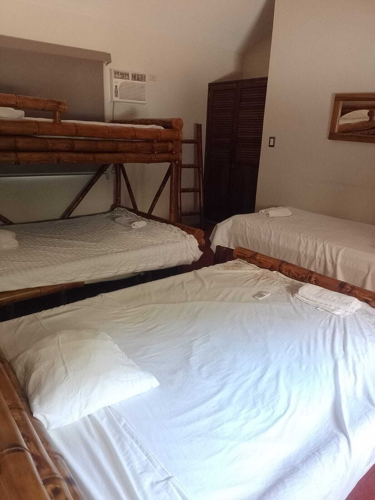 A dormitory room with bunk beds and a single bed. There is a window with blinds, a heater, and a wardrobe.