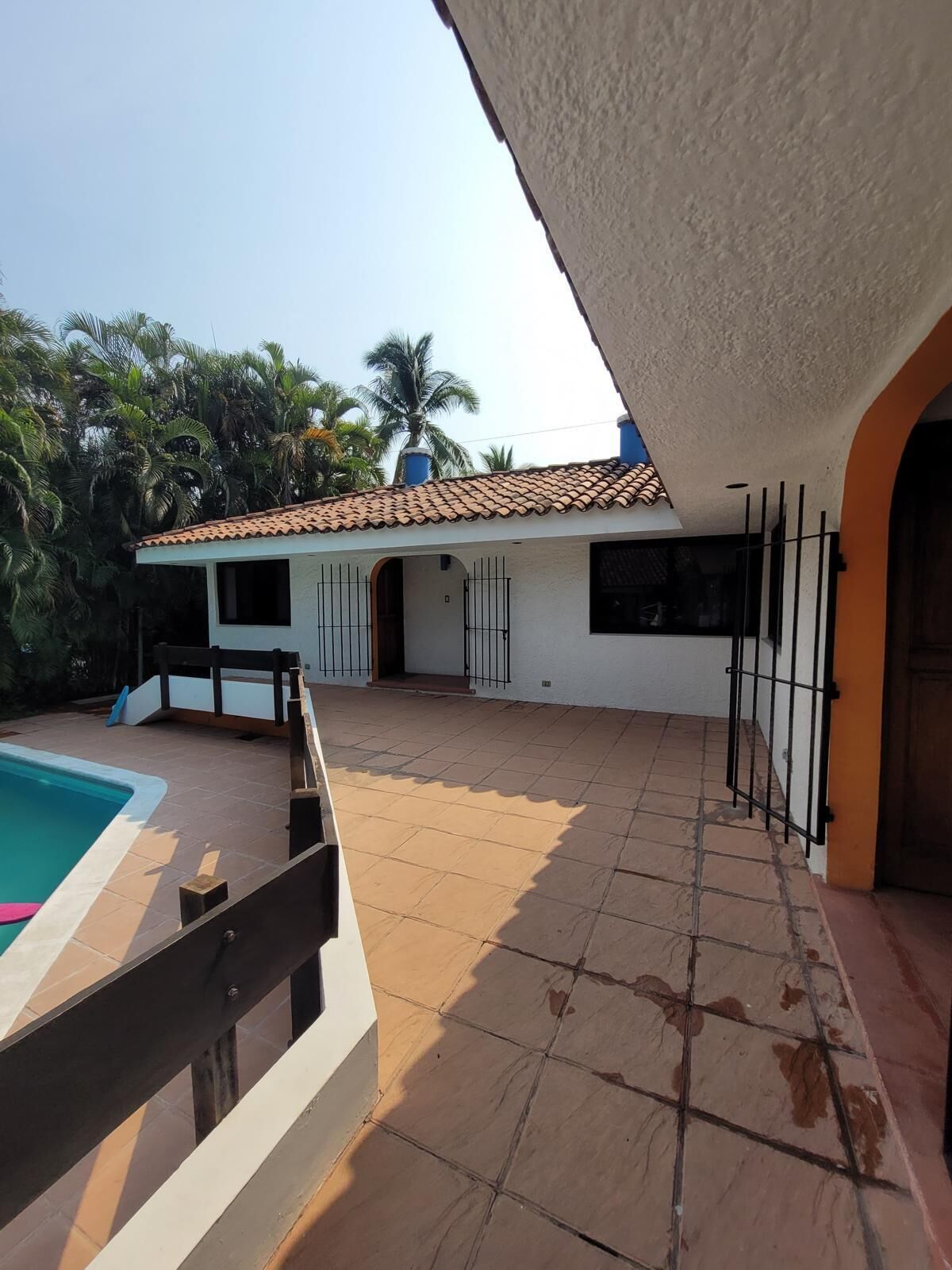 A house with a tiled patio, a swimming pool, and a view of palm trees.