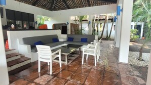 Une terrasse extérieure dotée d’un sol carrelé, d’un plafond en bois et de mobilier blanc.