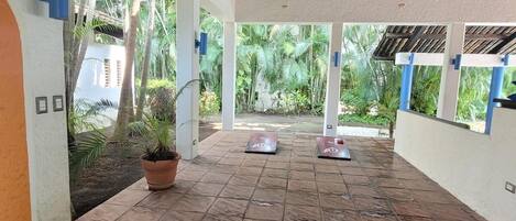 A covered outdoor area with tiled flooring, potted plants, and a view of greenery.