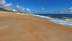 Ein Strand mit sandigem Ufer, vereinzelten Fußabdrücken und einem Gebäude im Hintergrund.