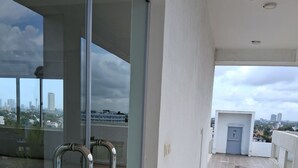 Un balcone con ringhiere in metallo, pavimento piastrellato e vista sulla città attraverso una porta in vetro.