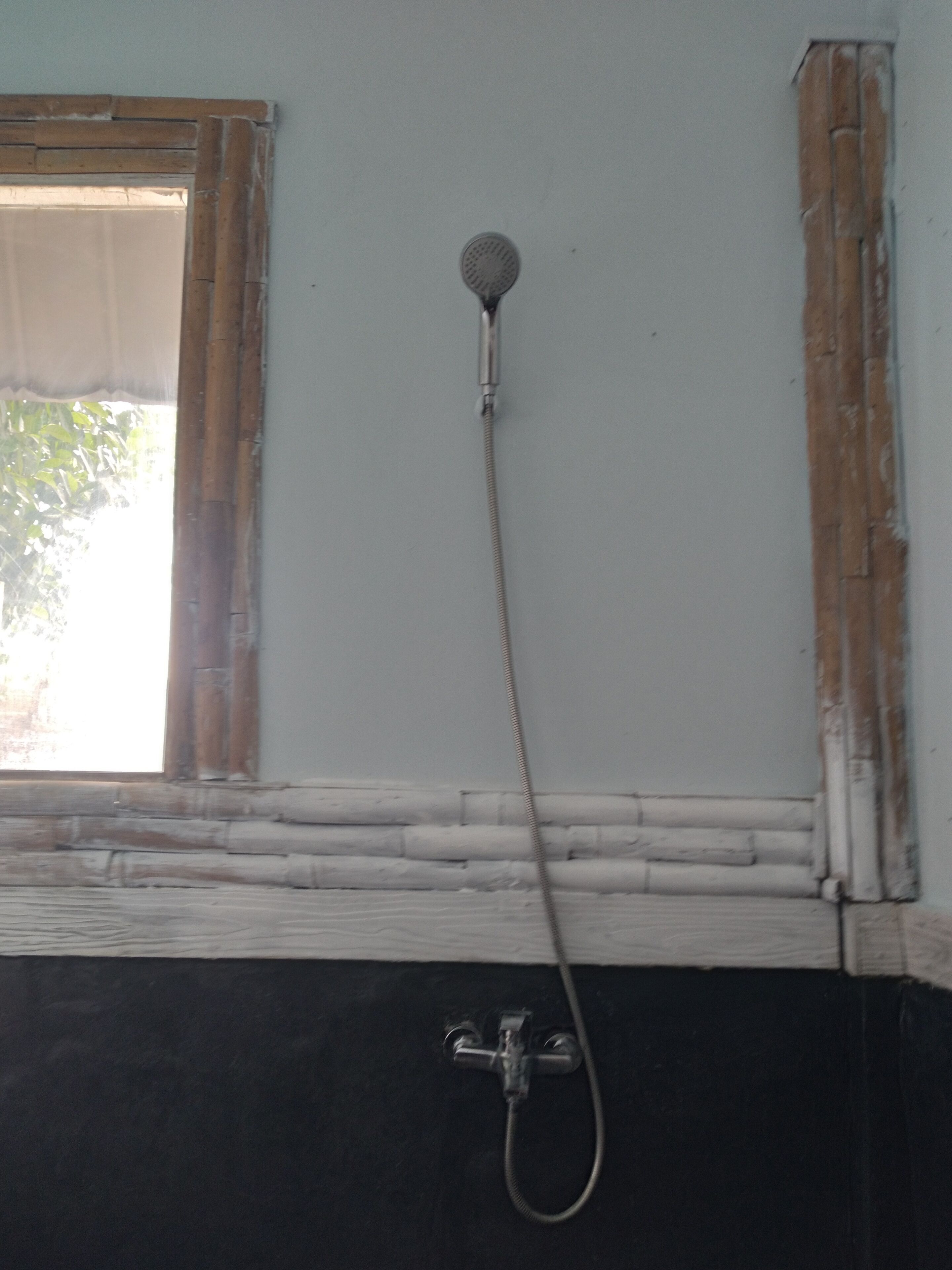 A bathroom with a shower head mounted on the wall, a window with a wooden frame, and a black and white tiled floor.