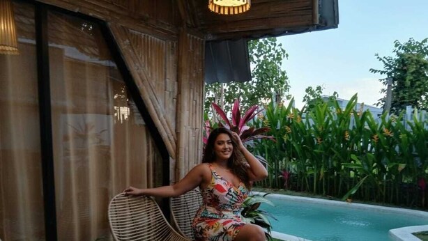 A person sitting on a wicker chair by a poolside, with a potted plant and a small table nearby. - Rustic 2 bedrooms villa near Obsidian Gym (Bali)